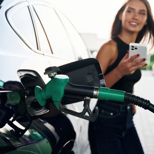 Waiting,,Holding,Smartphone.,A,Young,Woman,At,A,Gas,Station Se você também está em busca de uma solução para economizar, conheça o ClubAbis: um clube de benefícios exclusivo que oferece vantagens significativas para clientes da nossa proteção veicular.